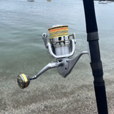 Close-up of a spinning fishing reel on a rod by the water, ReelsDeal Fishing Sale NZ